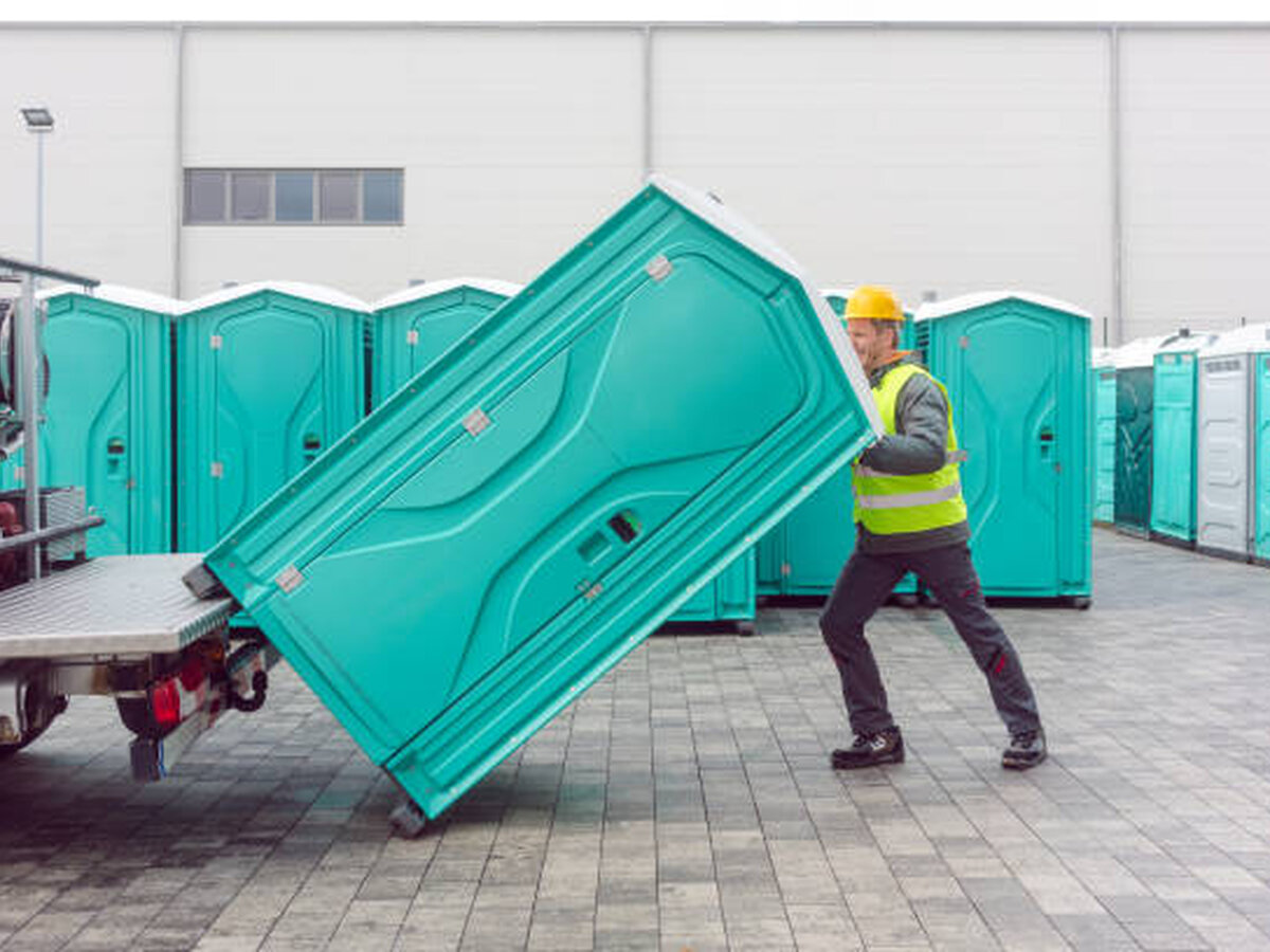 Crew member carefully positioning a portable restroom for an event